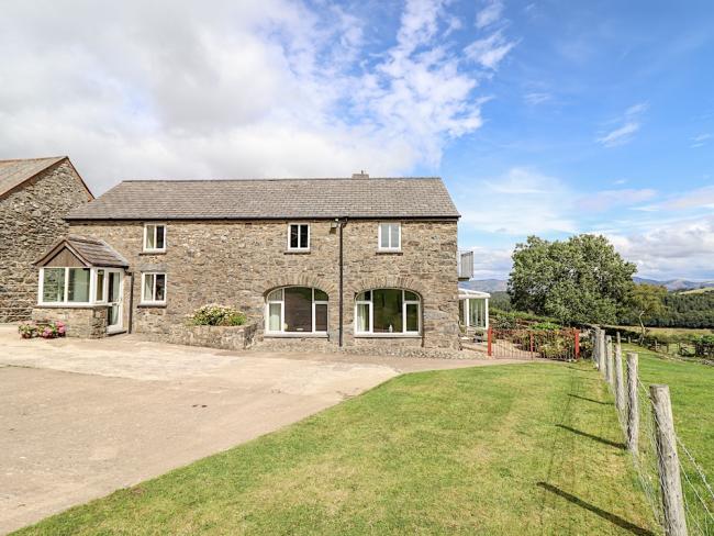 A 2-storey barn conversion overlooks a paved courtyard and open countryside in North Wales.