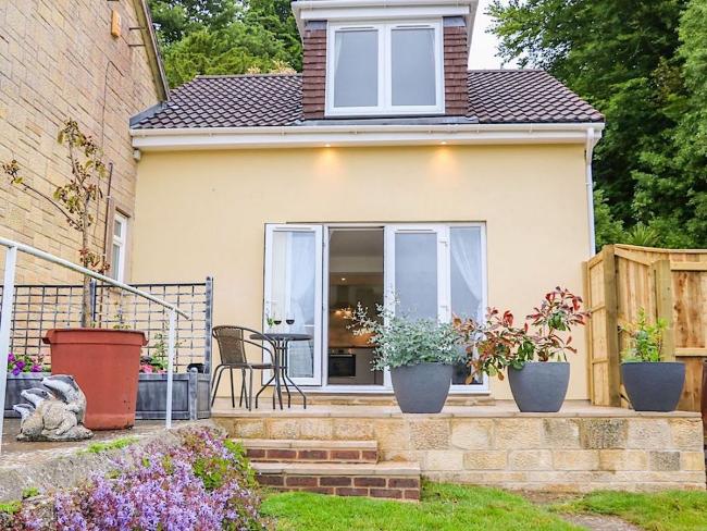 A semi-detached chalet bungalow with French Windows onto a patio with steps down to a flower-lined lawn.