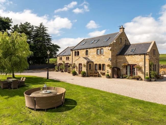 Exterior of a large stone-built Dales farmhouse with 2 wings, a large lawn and fields all around it.