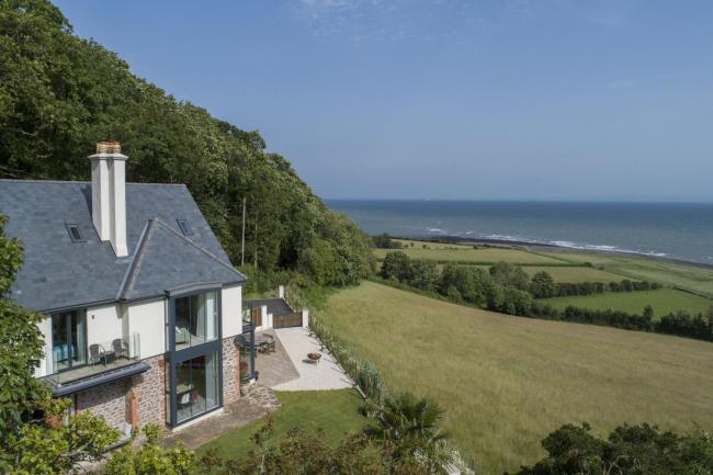 A large contemporary holiday cottage overlooks fields dipping down to a beach and ocean views.