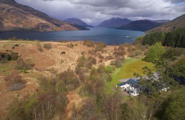 Aerial photo of a Loch in the Scottish Highlands with a holiday cottage in the foreground.