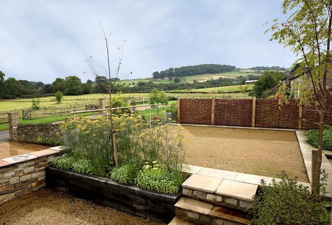 A cottage garden with rural views of hills and open countryside beyond a hedge.