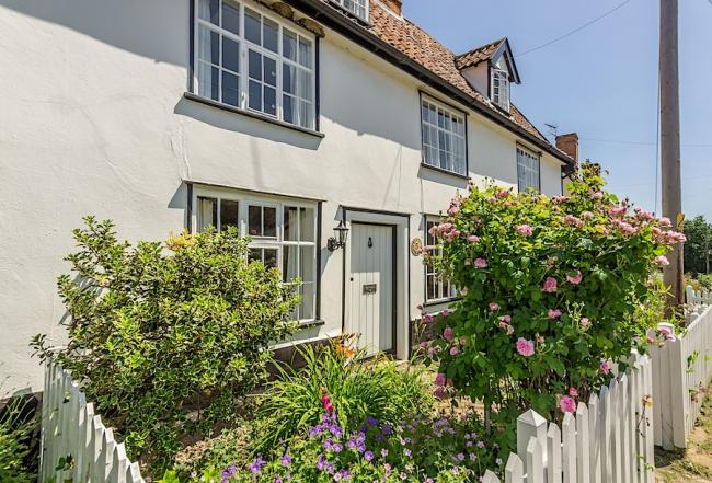 A double-fronted Sussex cottage with a flower-filled front garden behind a low picket fence.