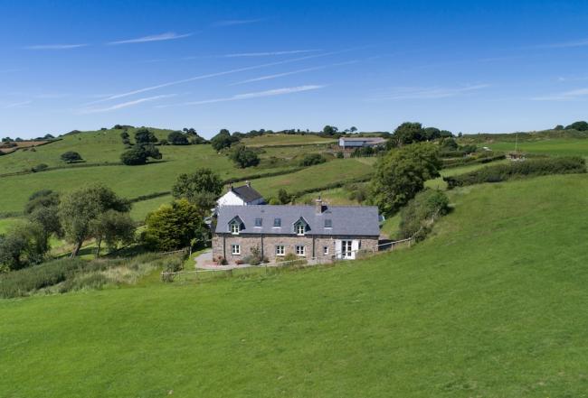 A 2-storey stone-built holiday cottage nestles in a fold a rural landscape.