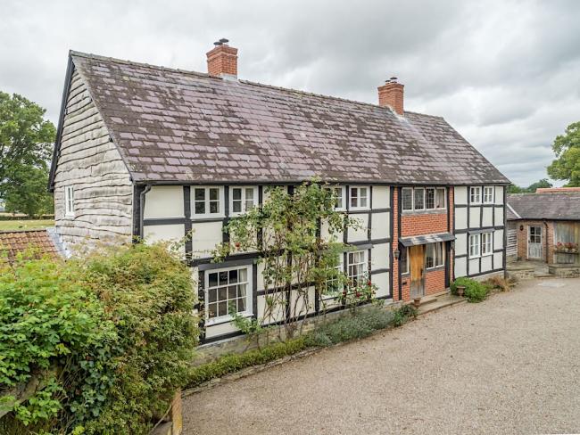 Exterior of a cross-timbered cottage overlooking a large shingle parking area.