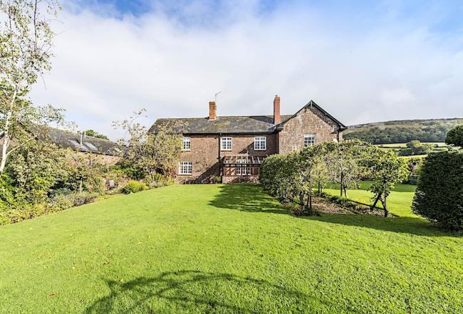 A stone cottage surrounded by fields overlooks a large garden with apple trees.