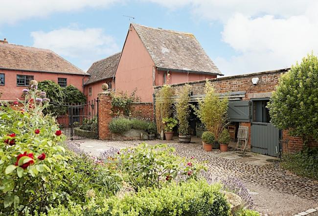 Exterior of a small Gloucestershire cottage and adjoining stable in a garden.
