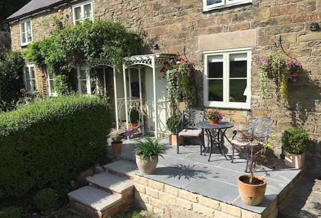 Stone-built exterior of a Peak District Cottage with flower-covered flagstone terrace.