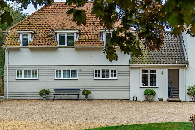 Clapper-board exterior of a 2-storey apartment with a terracotta roof and large courtyard. 