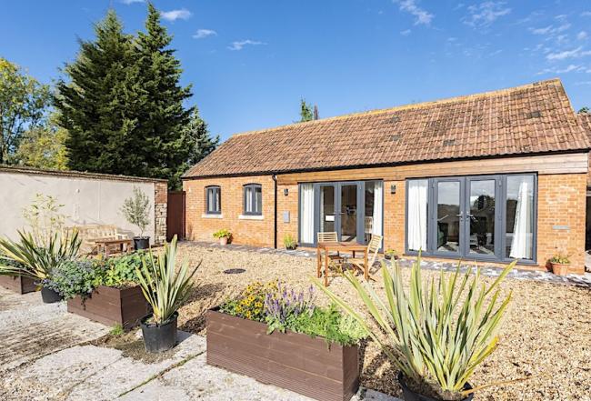 Single storey barn conversion with floor-to-ceiling French windows and a courtyard with raised flower beds.