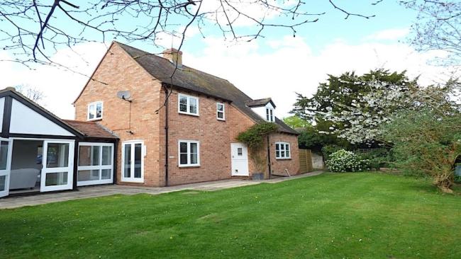 A brick-built holiday home with single storey extensions and a large, tree-lined and well-mown lawn