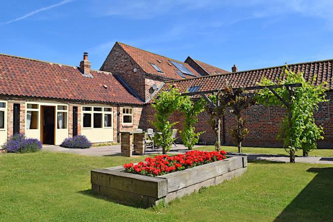 Barn conversion buildings overlooking a grass courtyard with a raised flower bed.
