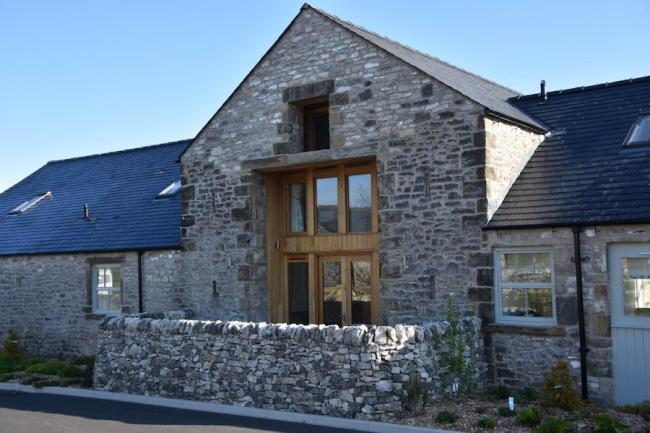 Exterior of a stone-built barn conversion with floor-to-ceiling windows behind a low stone wall.