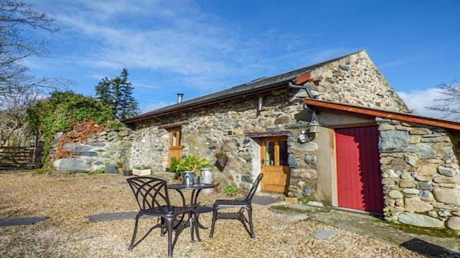 Exterior of a stone built barn conversion overlooking a  courtyard with dining table and chairs.