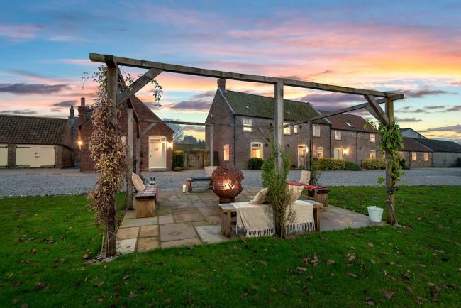 Exterior of a farm cottage and patio with a firepit at sunset.