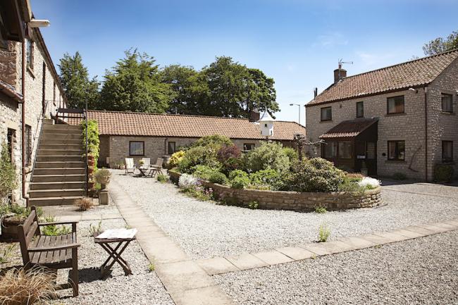 Barn conversions in a courtyard overlook a raised flower bed in its centre