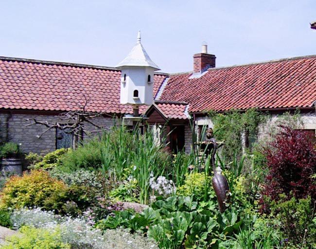 Exterior ofa barn conversion behind a shrub-filled garden.