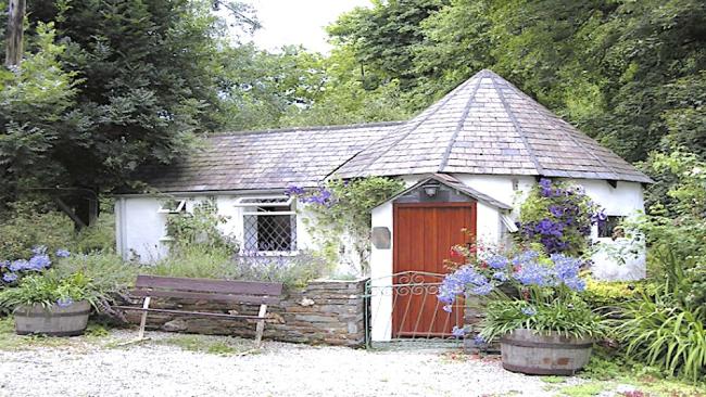 Exterior of a single-storey Cornish cottage surrouded by a tree-lined garden.