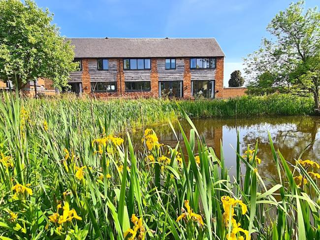 A reed-fringed lake sits in front of a 2-storey Shropshire barn conversion.