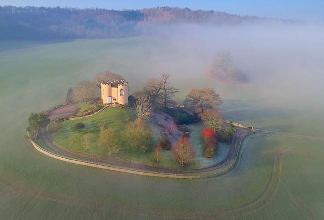 A mock Shropshire castle on a small hillock surrounded by a stone wall and open fields.