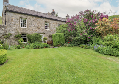 A large stone-built farmhouse overlooks a secure lawn and flower beds.