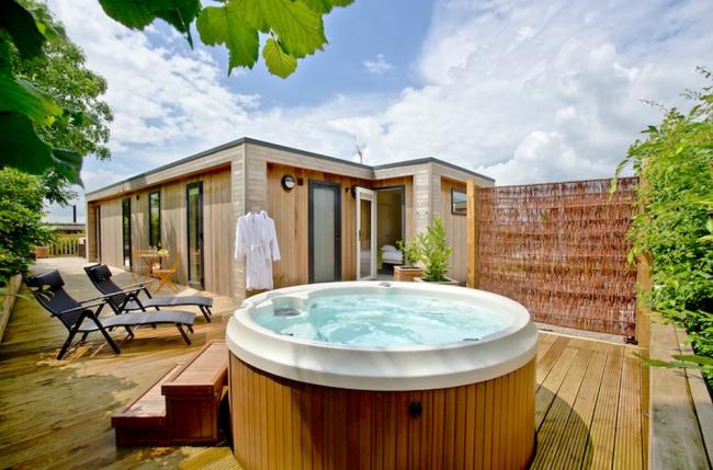 Exterior of a wooden eco lodge with a hot tub on its deck.