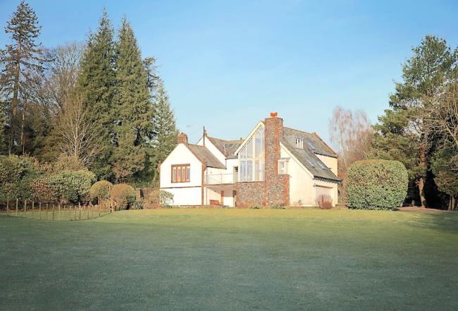 A twin-gabled house overlooks a large lawn bordered by a tall hedge.