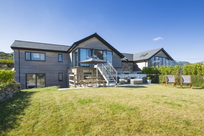 Exterior of a large timber lodge with a spacious deck overlooking an equally spacious, secure lawn.