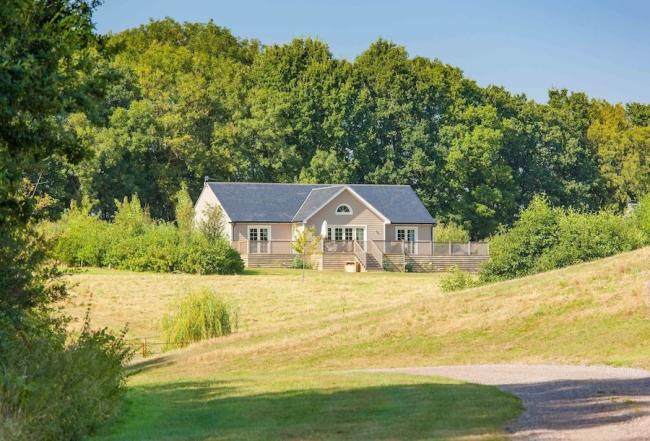 A timbered eco-lodge sits in front of mature woods overlooking open fields.