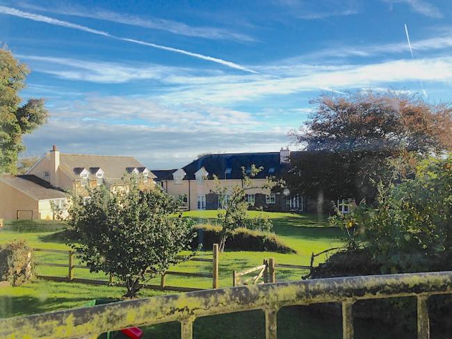 A large lawn with apple trees has a row of farm cottages in the background.