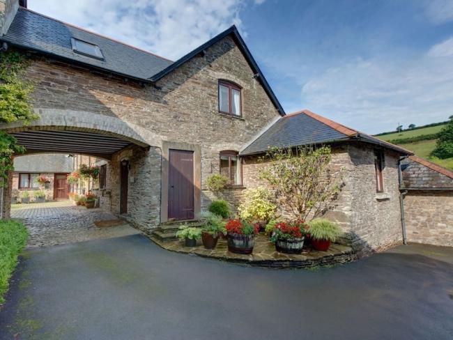 A stone-built cottage with a first floor that forms an arch over a driveway to a courtyard.