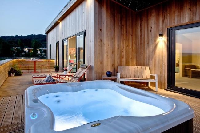 A hot tub and sunloungers on the deck of an timber eco lodge.