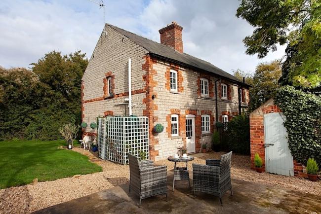 Exterior of a brick-built country cottage with a patio dining set on its courtyard.