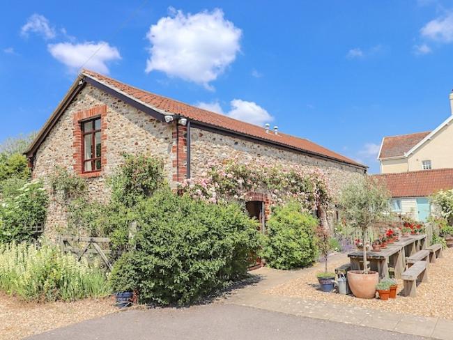 Exterior of a barn conversion with tables and chairs in a flower-filled courtyard.