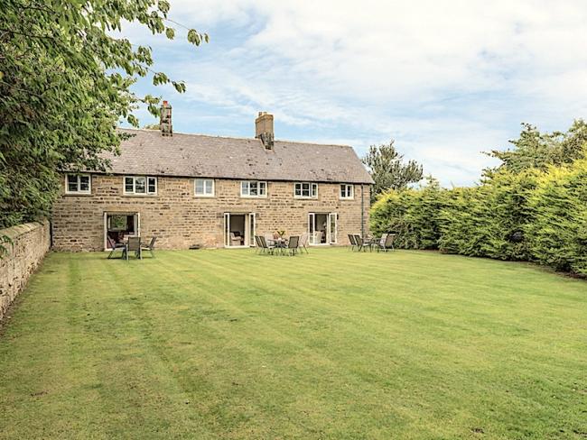 A long, stone-built cottage with 3 floor-to-ceiling ground-floor windows overlooking a spacious lawn. 