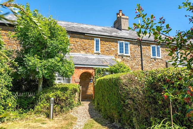 A footpath flanked by privet hedges leads to a stone-built holiday cottage with a covered porch.
