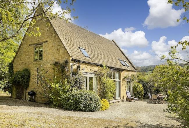 Cotswold Barn conversion surrounded by trees and shrubs.