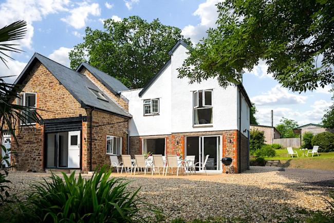 A twin-gabled holiday cottage nestles between two tall trees.