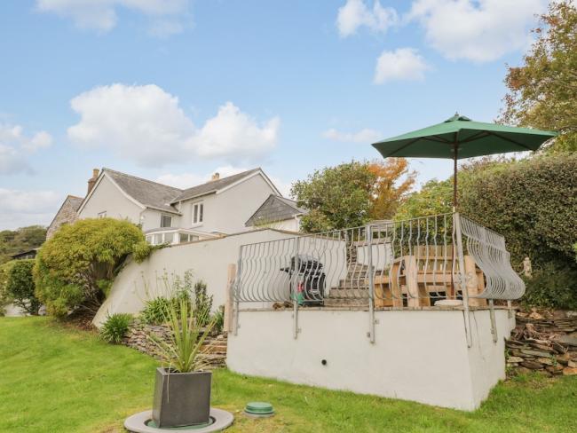 Exterior of a large contemporary house with a raised terrace and surrounded by mature gardens.