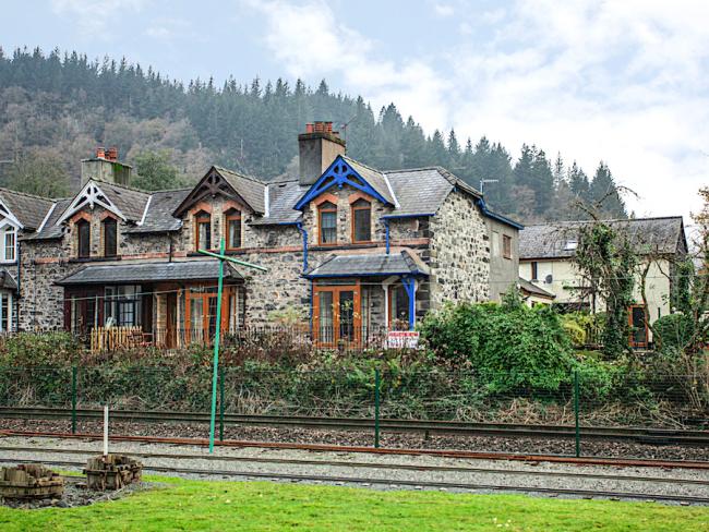 A twin gabled house with bay windows overlooks a railway line and fields.