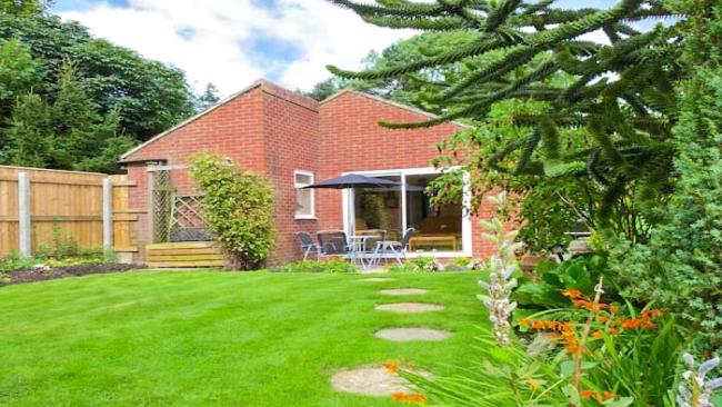 Rear exterior of a bungalow overlooking a tree-lined lawn.