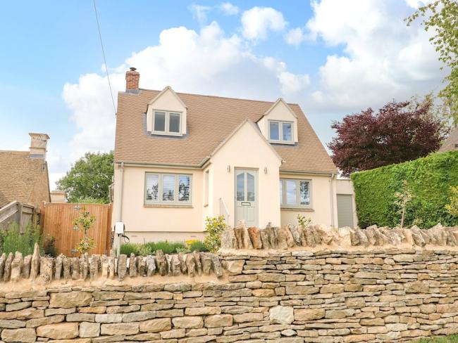 Exterior of a contemporary detached village house behind a dry stone wall.