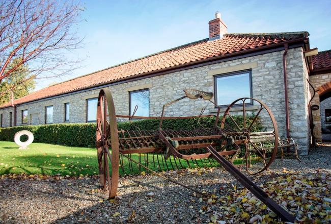 A large, single storey barn conversion overlooks a lawn.