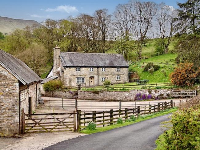 A pair of slate-roofed stone cottages in Herefordshire with large gardens overlook a country lane.