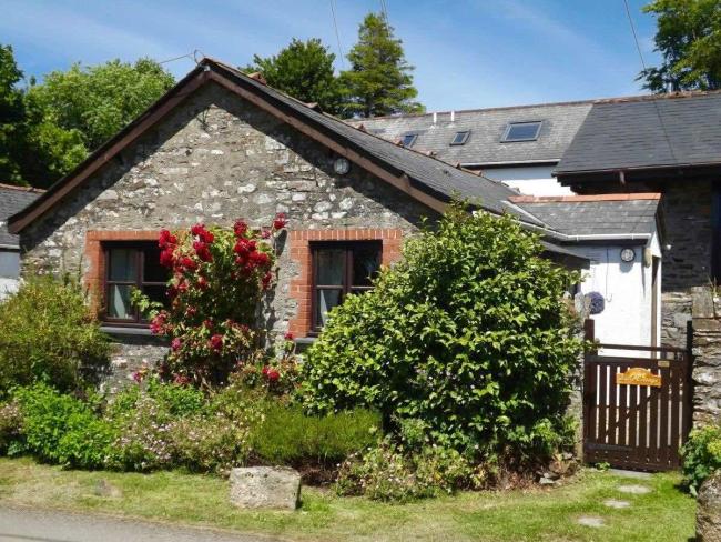 Stone-built, gable end of a cottage with flowering shrubs.