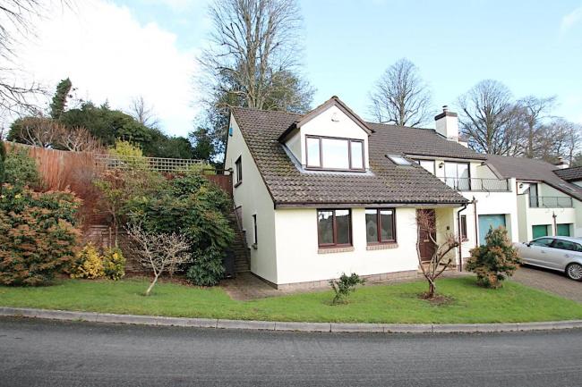 A modern 2-storey Exmoor house with a glass-fronted balcony and a lawn dotted with small trees