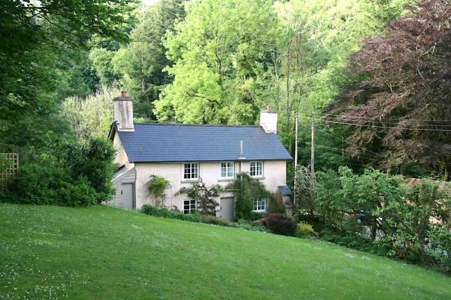 Double-fronted cottage with large lawn surrounded by mature trees.