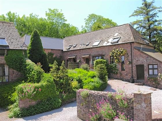 exmoor barn conversion overlooks a shrub-filled garden and drive.
