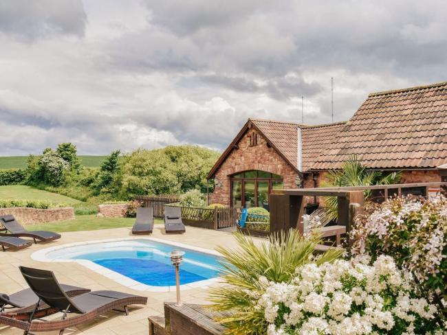 A stone barn conversion overlooks an outdoor swimming pool in a shrub-filled garden