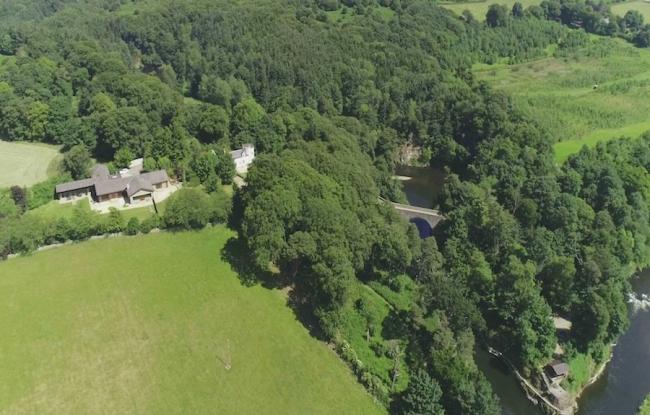 Aerial photo of a large holiday home nestling between mature woodland and fields overlooking a wide river.